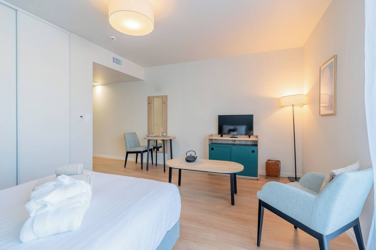 A hotel room with a bed, a desk, a chair, a TV, and a lamp.