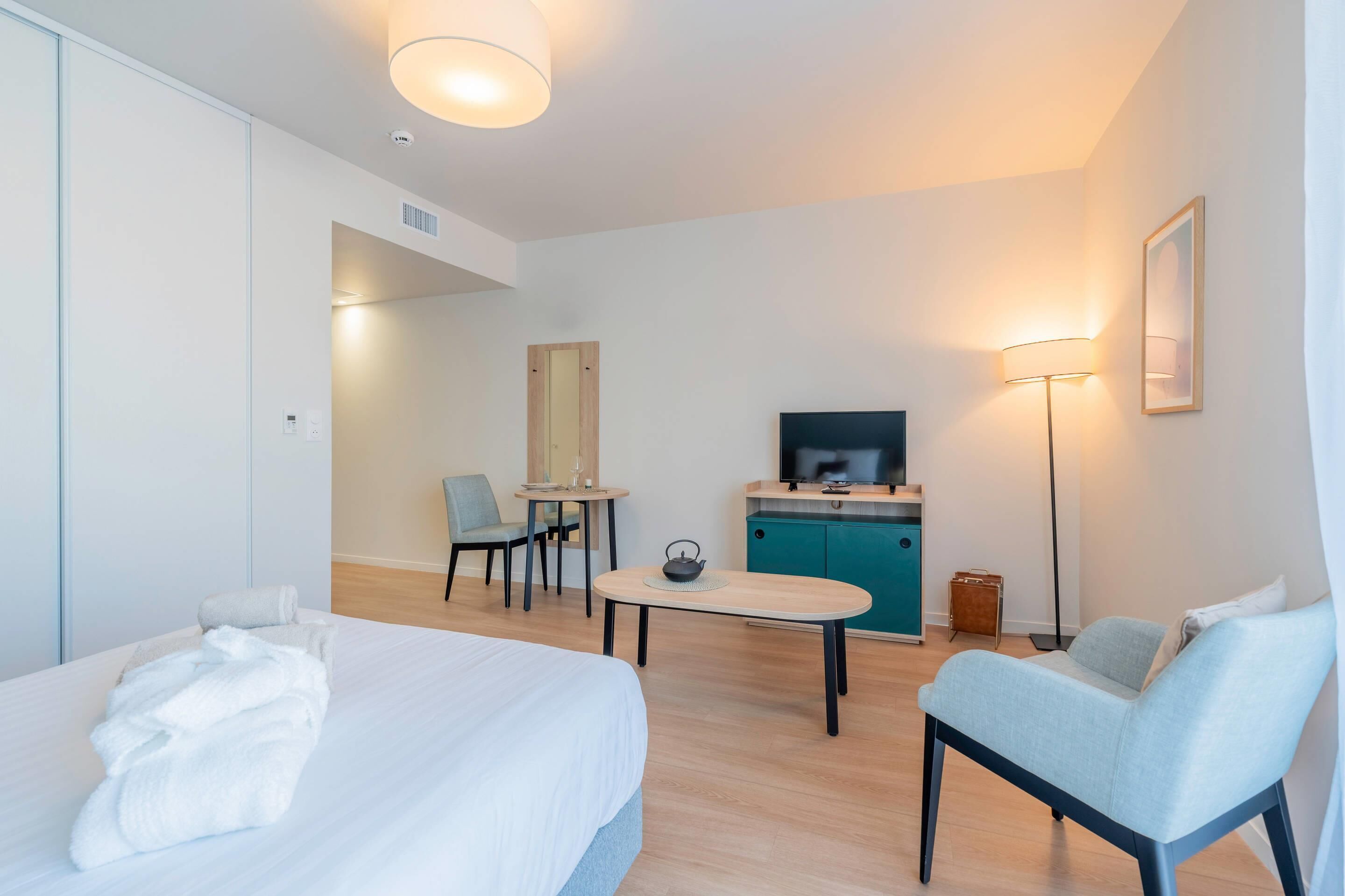 A modern hotel room with a bed, a desk, a chair, a TV, and a sofa.