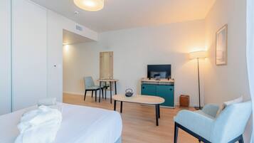 A hotel room with a bed, a desk, a chair, a TV, and a lamp.