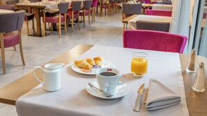 A dining area with tables, chairs, and a breakfast setting including croissants, coffee, and orange juice. - Quality Aparthotel Limoges (Limoges)