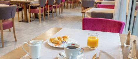 A dining area with tables, chairs, and a breakfast setting including croissants, coffee, and orange juice.