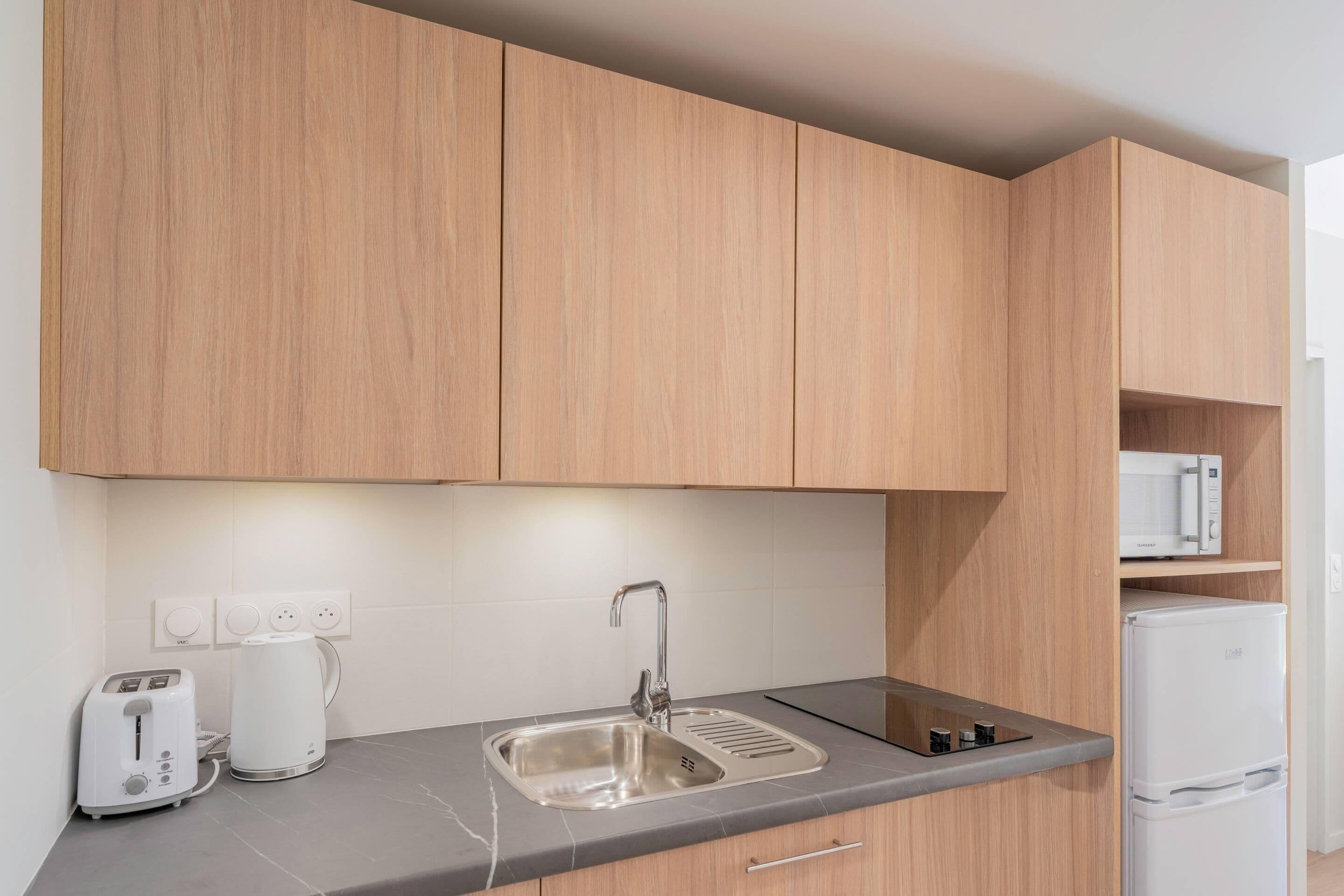 Una cocina moderna con armarios de madera, un lavamanos de acero inoxidable, un microondas integrado y un refrigerador blanco.