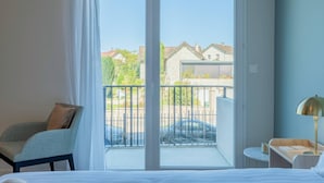 A hotel room with a bed, a chair, a small table with a lamp, and a balcony with a view of houses and a fence. - Quality Aparthotel Limoges (Limoges)