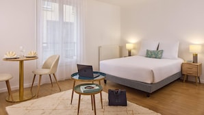 Ein Hotelzimmer mit einem Bett, Nachttischen, einem Laptop, einem Sessel, einem kleinen runden Tisch und einem Teppich.