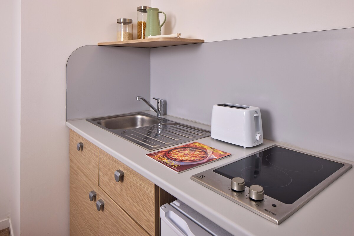 A compact kitchen with a sink, a toaster, a built-in induction cooktop, and a small shelf with jars.