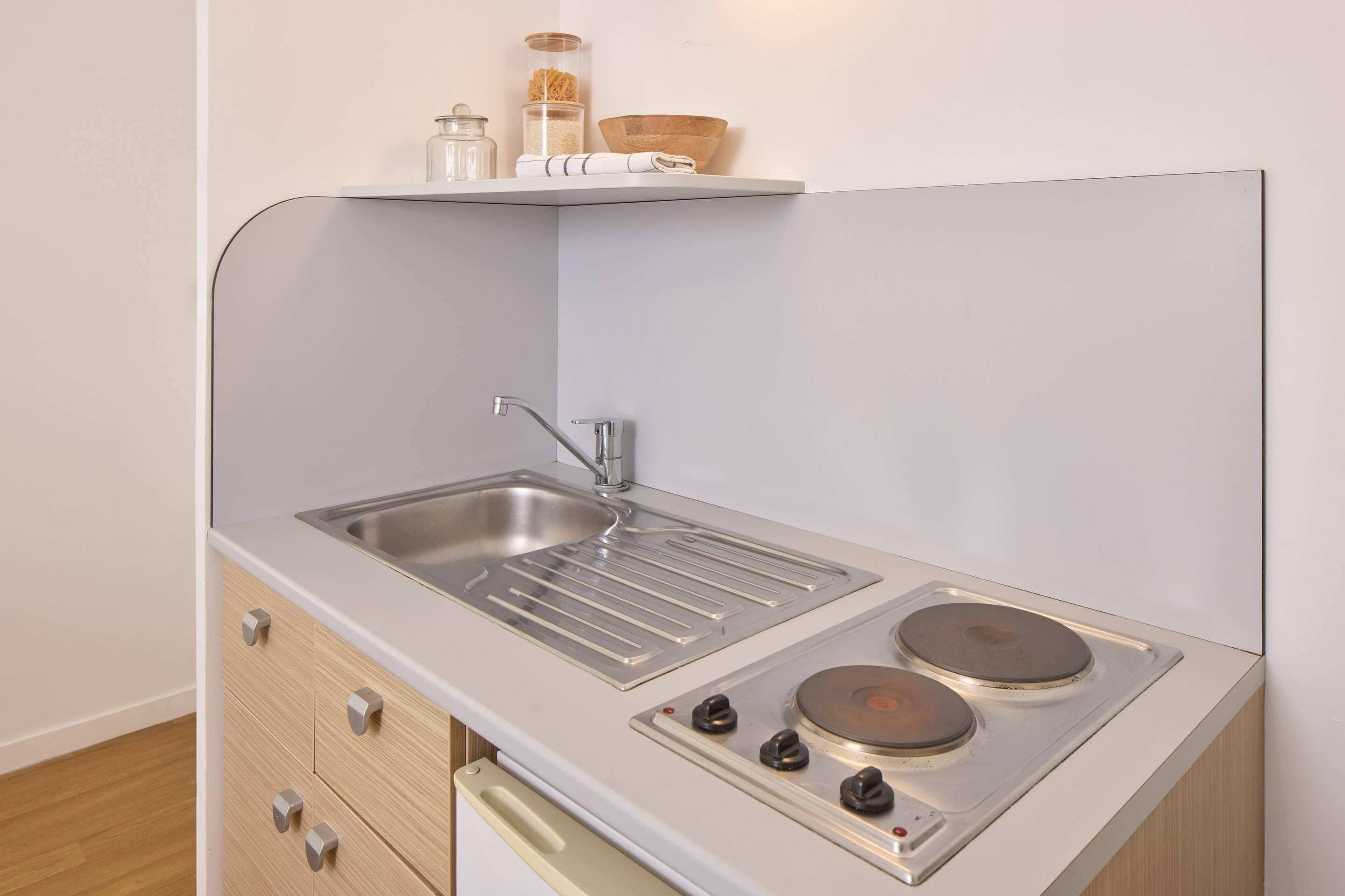 Une petite cuisine équipée avec un évier en acier inoxydable, une plaque de cuisson à deux foyers et une petite étagère au-dessus de l’évier.