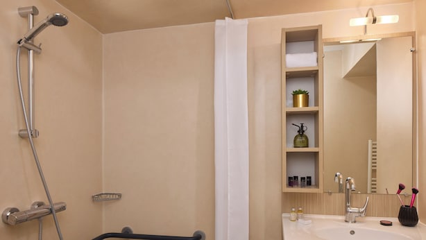 Ein Badezimmer mit Dusche, Waschbecken, Spiegel und Ablage für Pflegeprodukte.