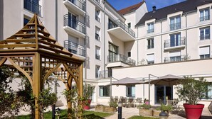 Ein mehrstöckiges Hotel mit Balkonen, Außenbestuhlung und einer Holzpergola.