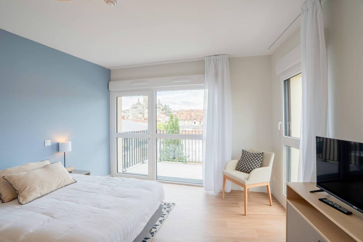 Una camera da letto con un letto, una sedia, una televisione e un balcone vista città.
