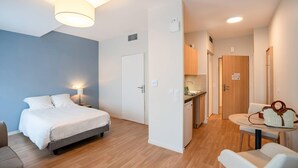 A modern hotel room with a bed, bedside table, lamp, and a view into the kitchen area. - Quality Aparthotel Périgueux (Perigueux)