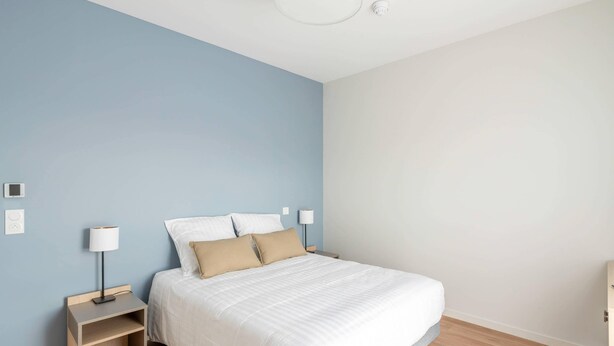 A bedroom with a bed, nightstands, and a ceiling light fixture. - Quality Aparthotel Périgueux (Perigueux)