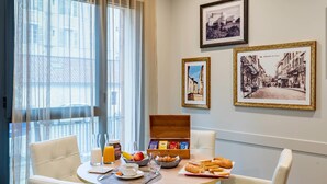A breakfast table with a fruit bowl, croissants, and a coffee cup. There are framed pictures on the wall and a window with curtains. - Quality Aparthotel Périgueux (Perigueux)
