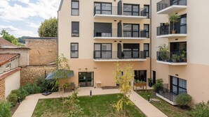 A multi-story residential building with balconies, a small courtyard, and a stone wall. - Quality Aparthotel Périgueux (Perigueux)
