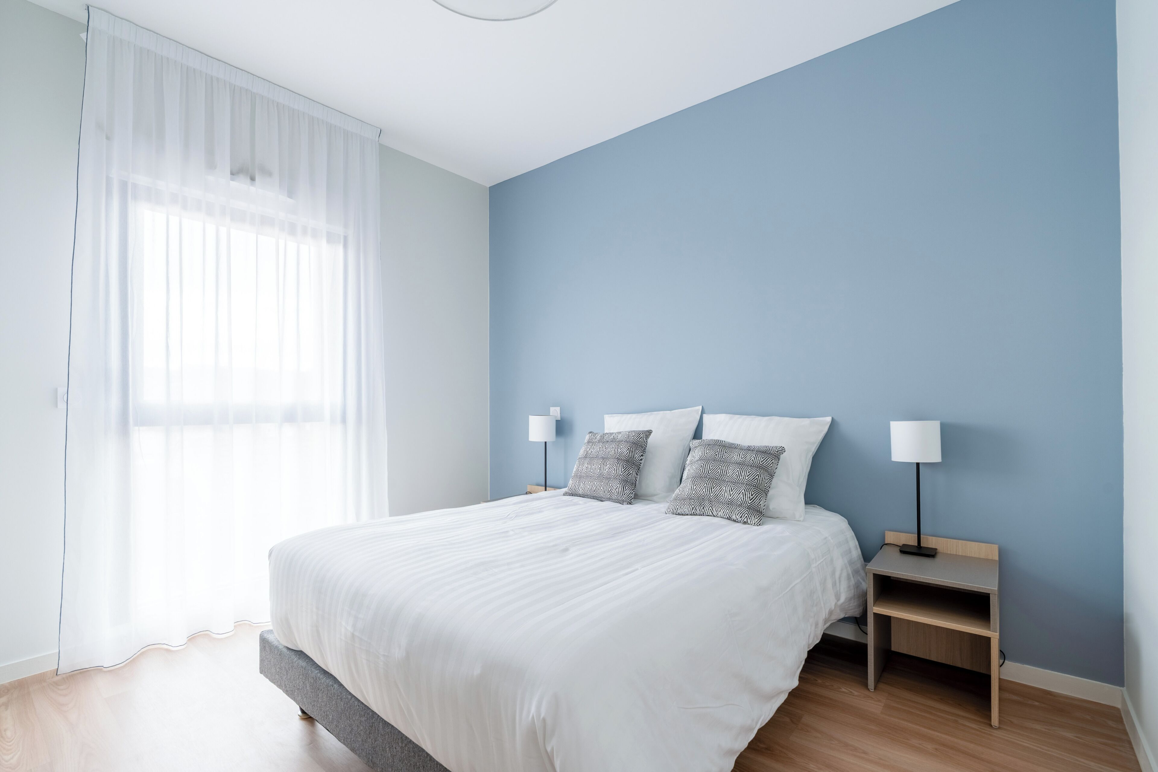 A bedroom with a bed, two bedside tables, and a window with sheer curtains.