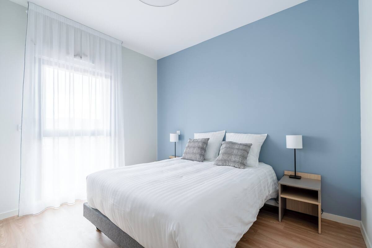 Una camera da letto con un letto, due comodini e una finestra con tende leggere.