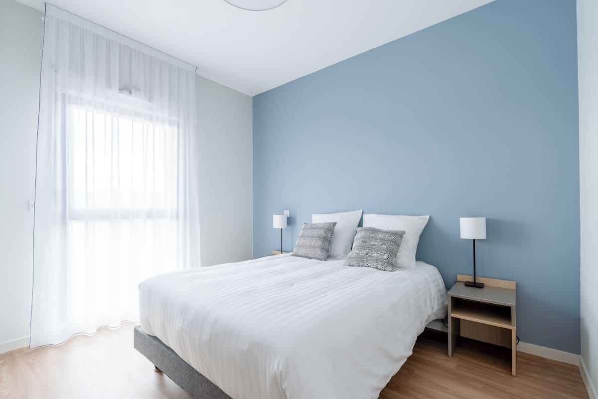 Un dormitorio con una cama, dos mesitas de noche y un ventanal con cortinas de encaje.