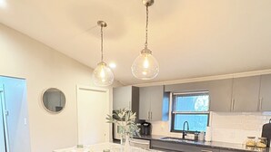 A modern kitchen with a central island, wooden stools, pendant lighting, and a view of the outdoors. - Tulsa Expo Luxury Stay - 1 mi to Expo (Tulsa)