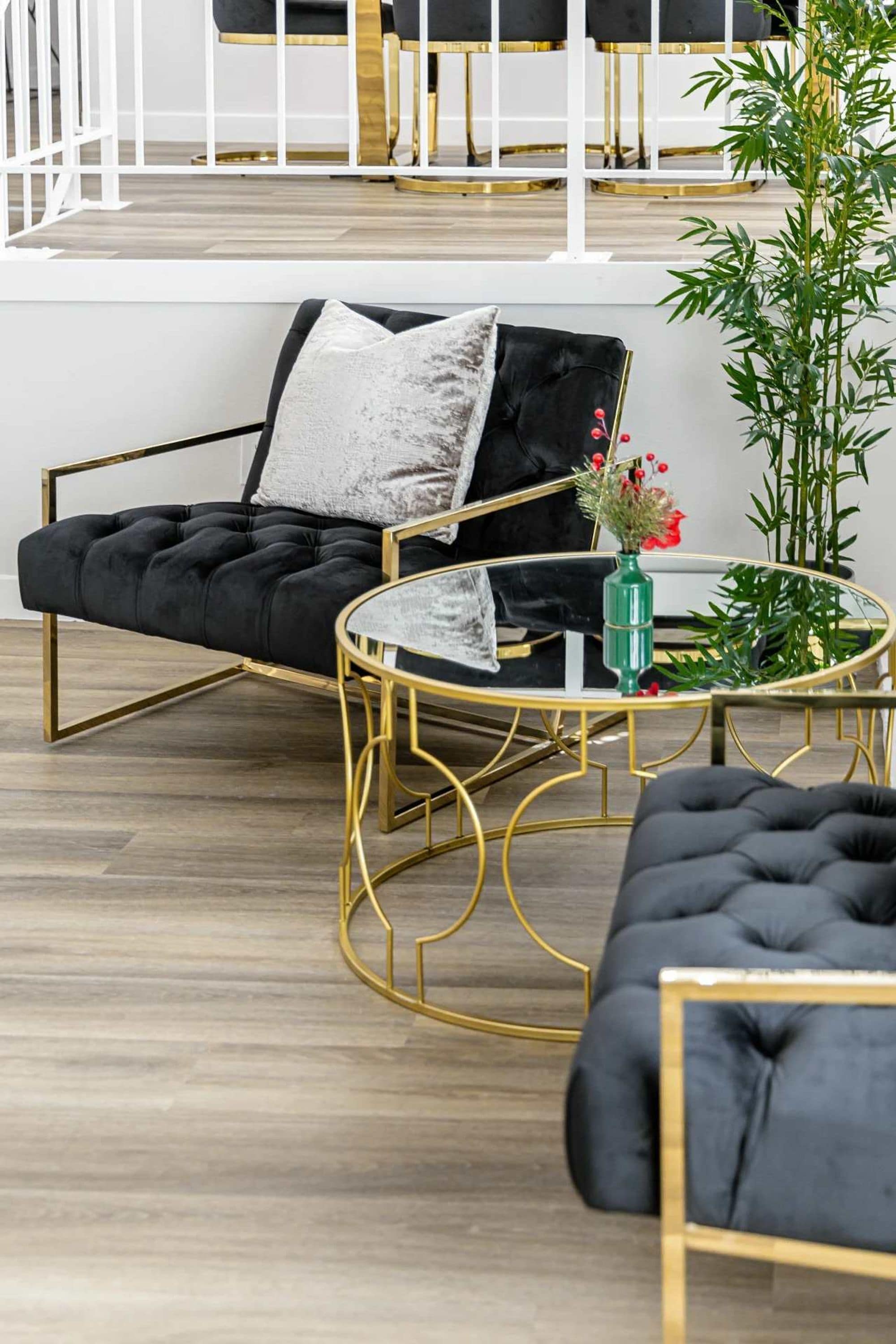 A modern living room with a black sofa, a round gold-framed coffee table, and a green vase with flowers.