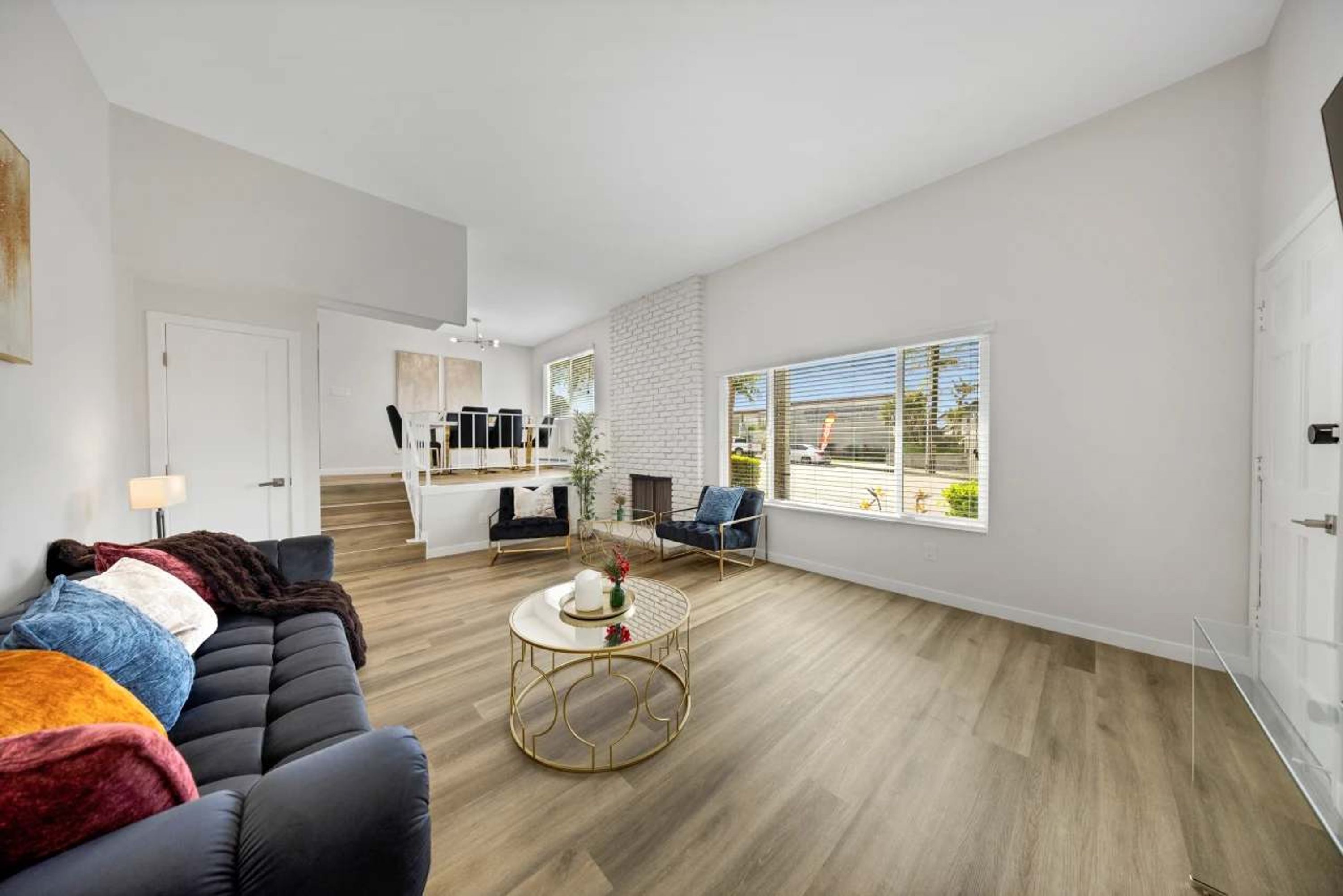 A modern living room with a black sofa, a round coffee table, and a dining area with a kitchen in the background.