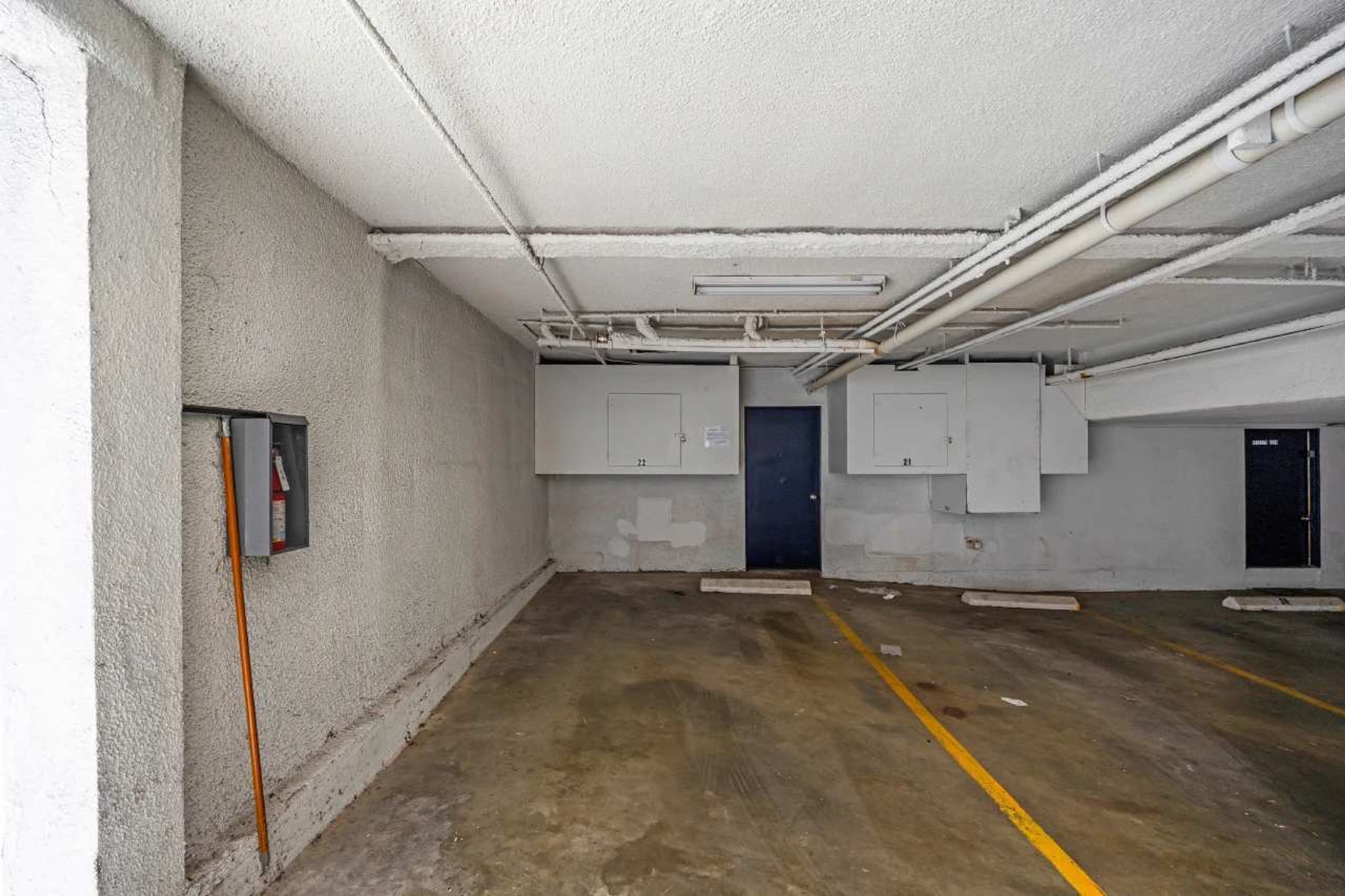 Un interior espacioso y sin terminar, con paredes de concreto, tuberías expuestas y suelo de concreto.