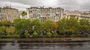 Ein mehrstöckiges Wohngebäude mit Balkonen, einem Parkplatz mit Autos und einem Fluss im Vordergrund.