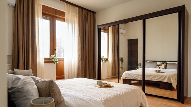 Ein Schlafzimmer mit einem großen Bett, einem Spiegel und einem Fenster mit Vorhängen.