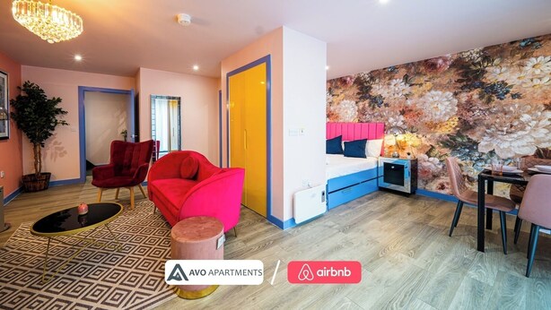 A modern apartment with a large bed, a dining area, and a living room with a red chair and a small table. - Comfortable Studio with Great City Access (Sheffield)
