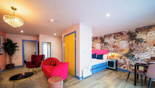 Un apartamento moderno con una cama grande, un comedor y una sala de estar con una silla roja y una mesita.