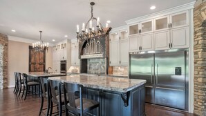A spacious kitchen with a large island, dark wooden bar stools, white cabinetry, a stainless steel refrigerator, and a stone accent wall.