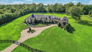 A large, multi-story stone house with a wrap-around driveway and a well-maintained lawn.