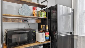 Een keuken met een magnetron, broodrooster en een koelkast. Er zijn planken met diverse spullen, waaronder een decoratie in de vorm van een hart, een pot en een koffiebus.