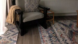 Una sala de estar con un sofá, un televisor montado en la pared, un ventanal con cortinas y un radiador.