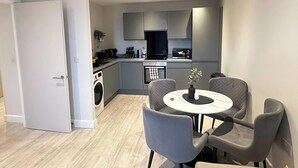 A modern kitchen with grey cabinets, a built-in oven, and a dining area with a round table and grey chairs.