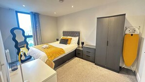 A modern bedroom with a large bed, a wardrobe, a desk, and a window with curtains.