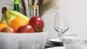 A dining table with a bowl of fruit, a wine glass, and a decorative wall clock.