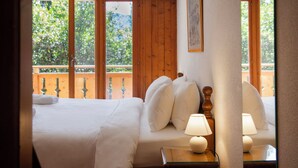 A bedroom with a bed, pillows, a bedside lamp, and a view of greenery through large windows.