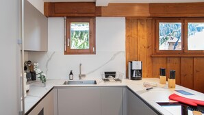 A modern kitchen with a built-in sink, wooden cabinets, a coffee maker, and a window with a view of a snowy landscape.