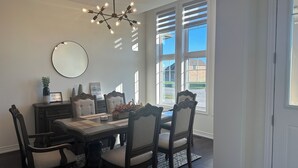 Ein Esszimmer mit einem dunklen Holztisch, gepolsterten Stühlen, einem Kronleuchter und Blick ins Freie durch große Fenster.