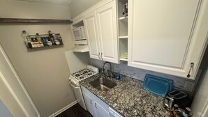 A compact kitchen with white cabinets, a gas stove, a sink, and a countertop with a blue cutting board. - Quiet Corner ATL (Atlanta)