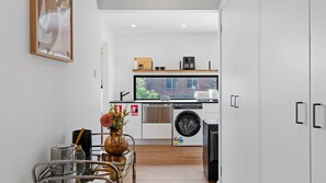 A modern kitchen with a washing machine, a coffee maker, and a window with a view of a brick building.