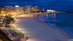A coastal cityscape at dusk with illuminated buildings, a beach, and a promenade. - The Jitterbug - Sleeping 4 Guests (The Hill)
