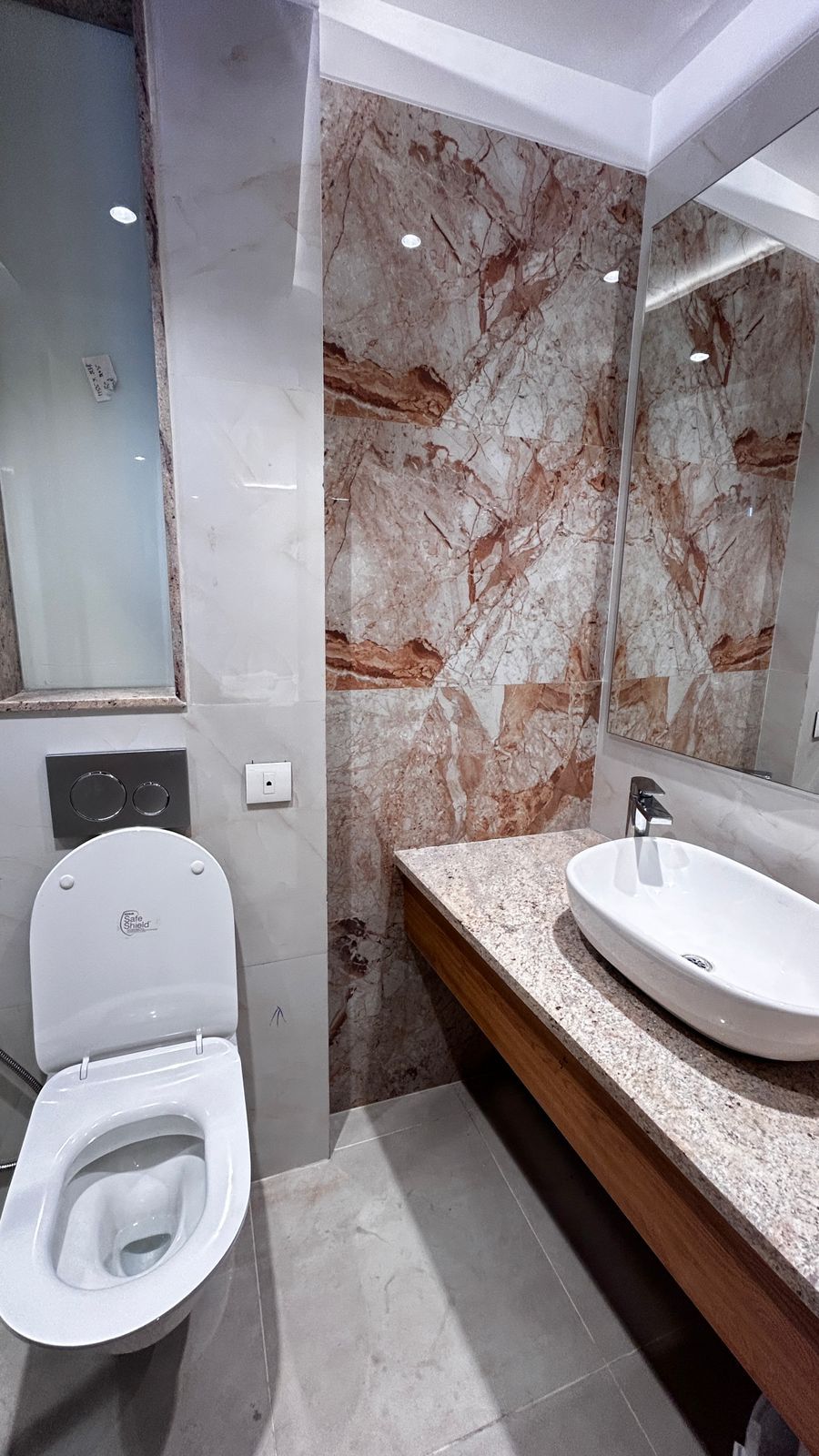 A modern bathroom with a marble wall, a toilet, and a sink with a mirror above it.