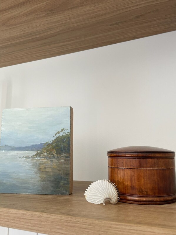 Una estantería de madera con un cuadro enmarco de un paisaje costero y una caja de madera con una concha marina.