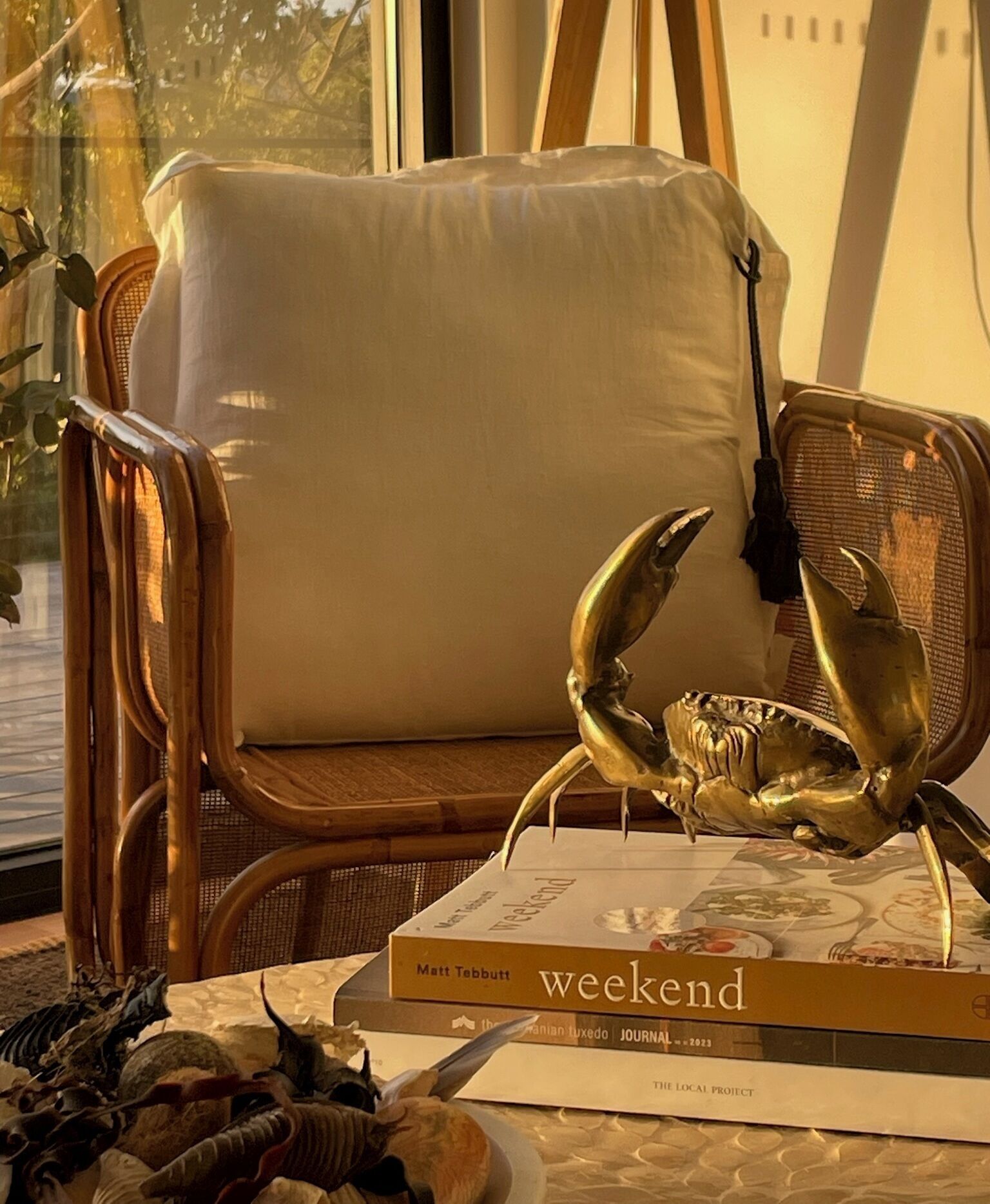 A wicker chair with a white cushion, a decorative crab, and a book titled 'Weekend' by Matt Tebbott.