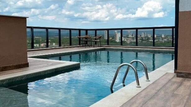 Uma piscina no terraço com vista desobstruída da paisagem urbana, um deck de madeira e um corrimão de metal.