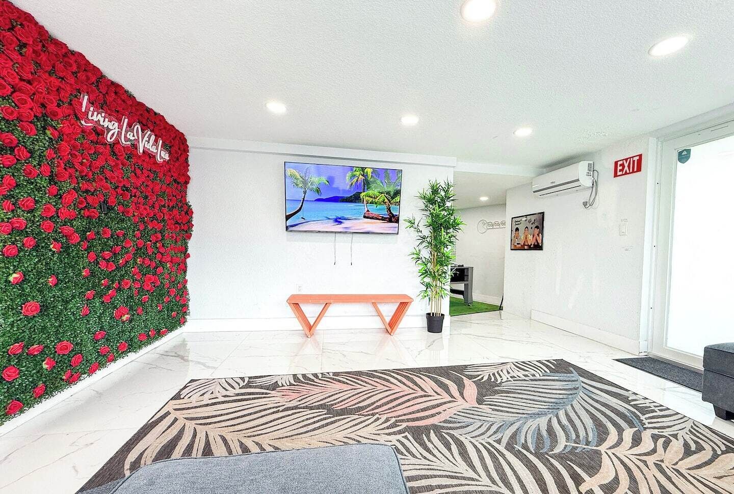 Un espace d’accueil moderne avec un mur décoré de motifs floraux rouges, un grand écran de télévision, un banc en bois et une moquette à motifs.