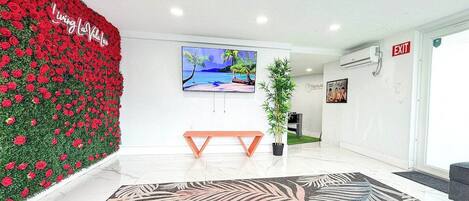 Un espace d’accueil moderne avec un mur décoré de motifs floraux rouges, un grand écran de télévision, un banc en bois et une moquette à motifs.