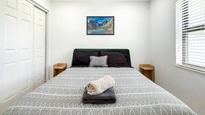 Ein ordentlich bezogenes Bett mit einem geometrisch gemusterten Überwurf, zwei Kissen und einem zusammengerollten Handtuch.