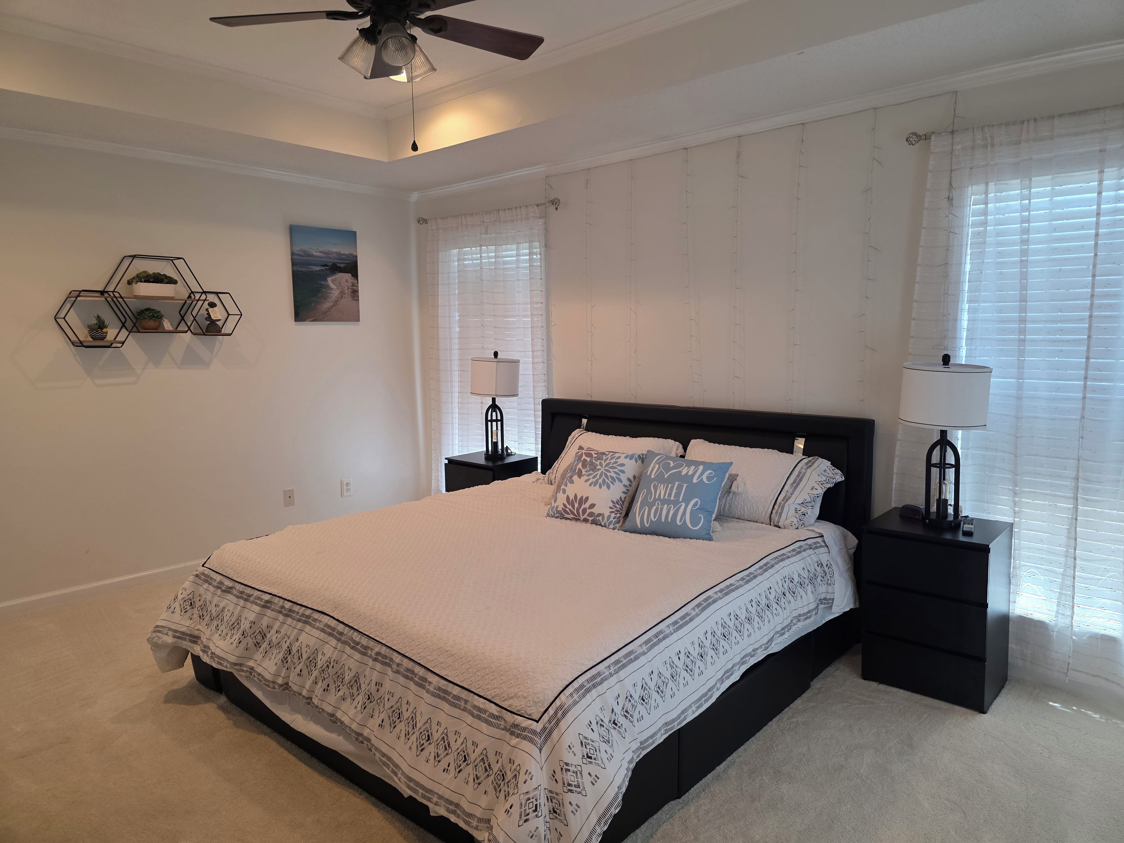 Une chambre à coucher avec un lit, des tables de chevet, un ventilateur de plafond et une fenêtre avec des stores.