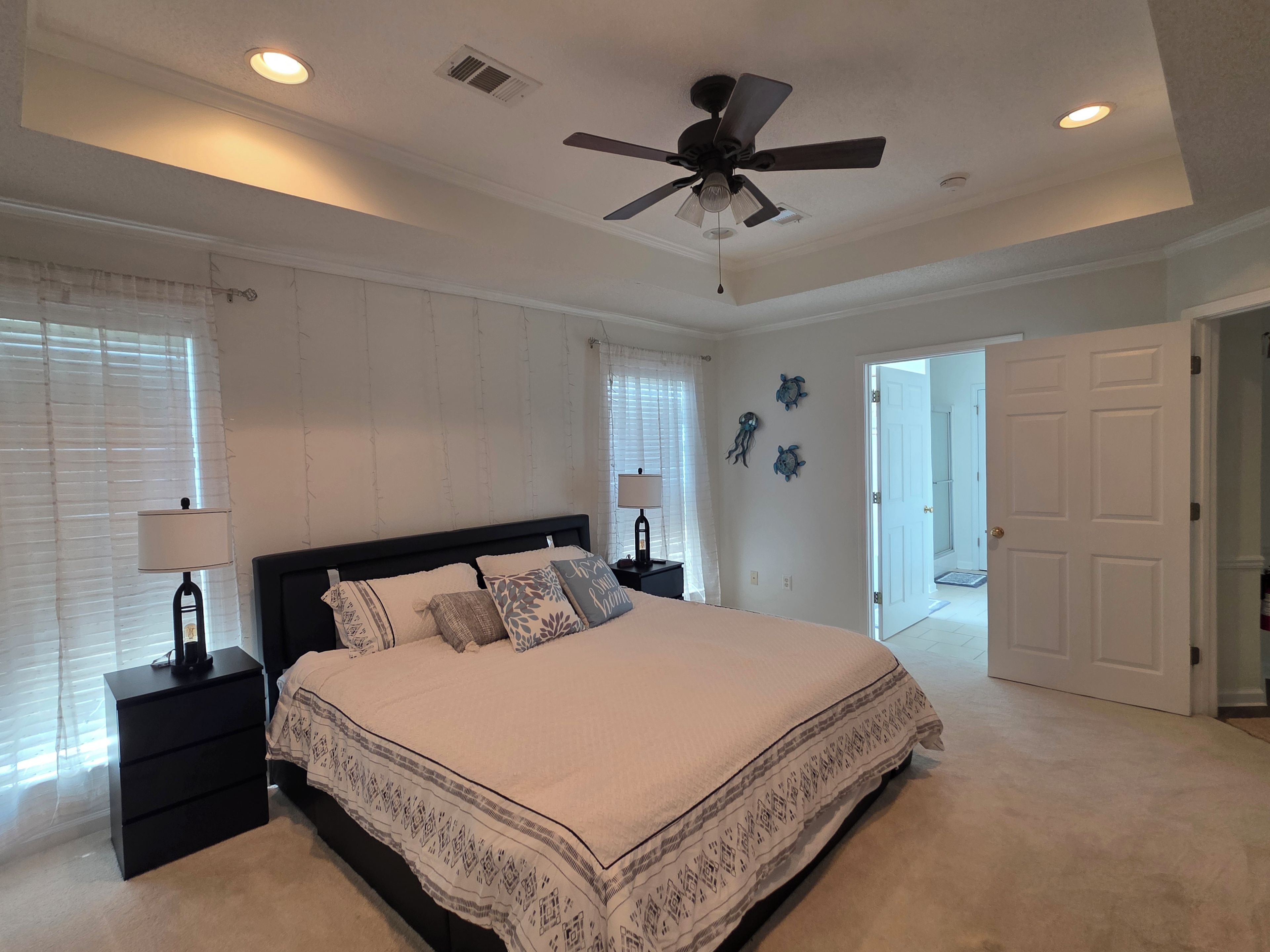 A bedroom with a bed, nightstands, a ceiling fan, and a door leading to another room.